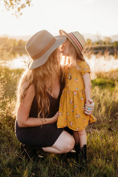 mom and daughter wearing hats at sunset by a lake  in Longmont Colorado