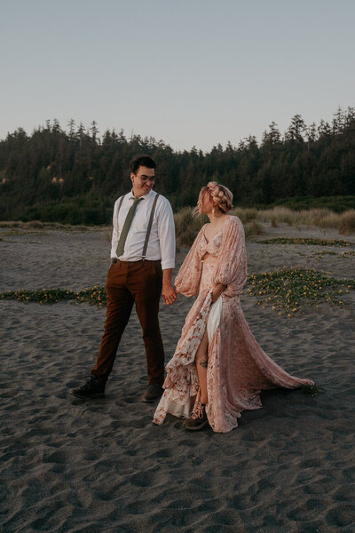 groom and bride wearing pink dress walk holding hands down the beach after elopement in Big Sur