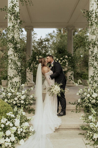 Bride and groom kissing at ceremony altar with greenery decor