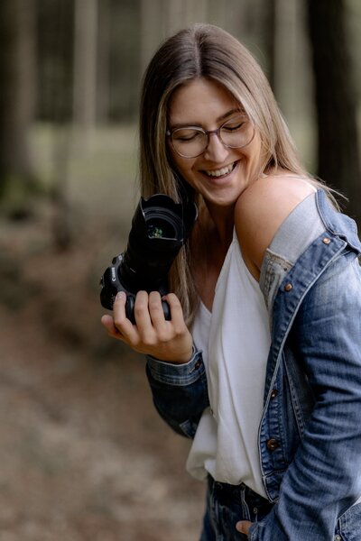 Lisa Winkelbauer steht mit Kamera in der Hand im Wald