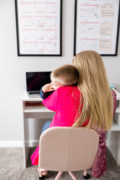 Mom dressed for work sitting at work desk while comforting her son.