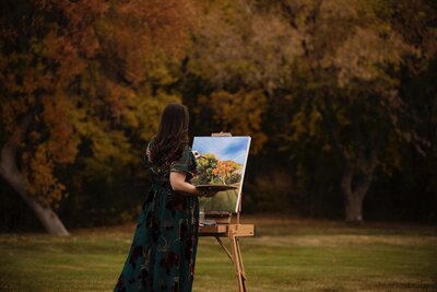 Debbie painting a landscape piece with her canvas on an easel.
