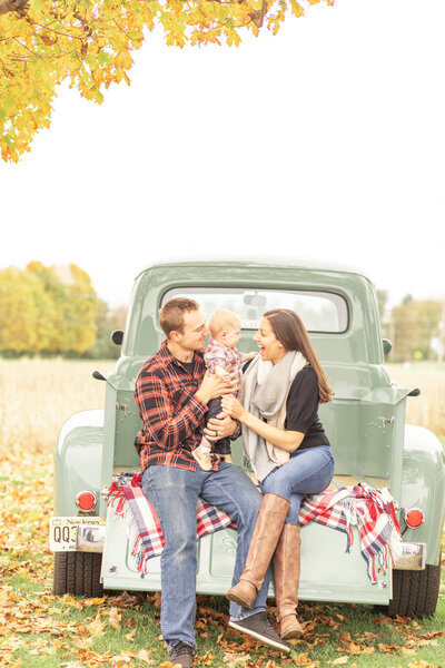 family of three little boy sitting on green vintage truck in fall