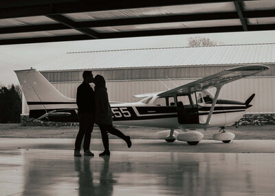 couples silhouette of them kissing with her leg up and there is an airplane in the background