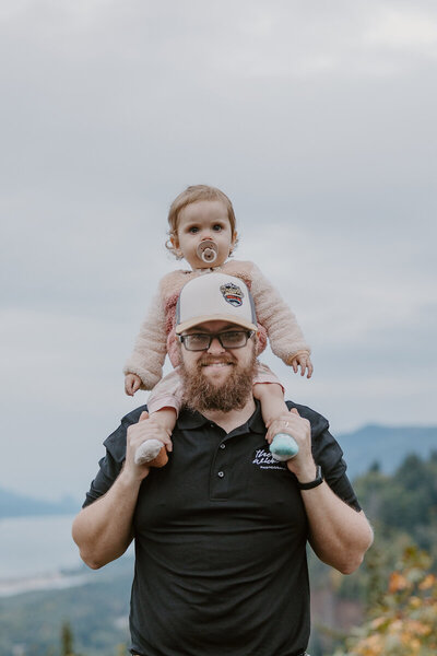Photographer Hunter Wickert stands on a mountain overlook with his toddler on his shoulders