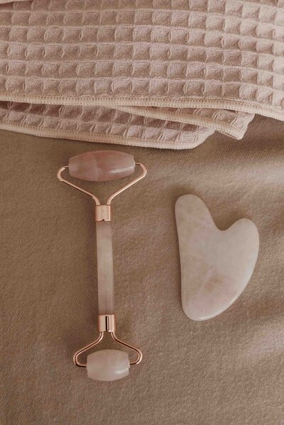 A rose quartz face roller and gua sha tool placed on a soft beige towel, creating a calming and luxurious self-care moment.