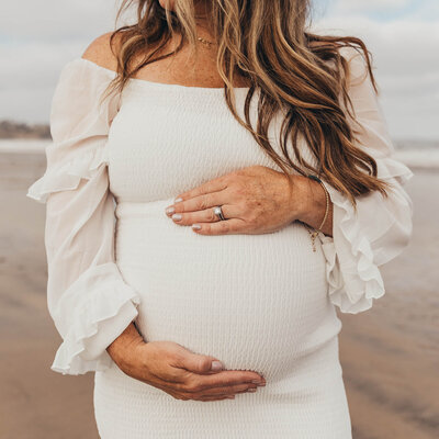 close up of a pregnant woman on the beach in San DIego holding her baby bump