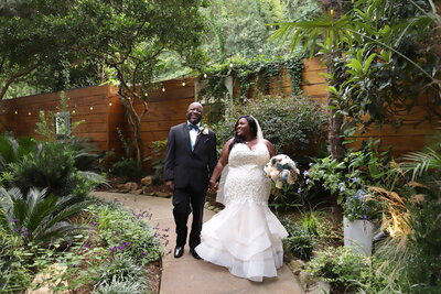 Black bride and groom holding hands while walking in the garden on their wedding day