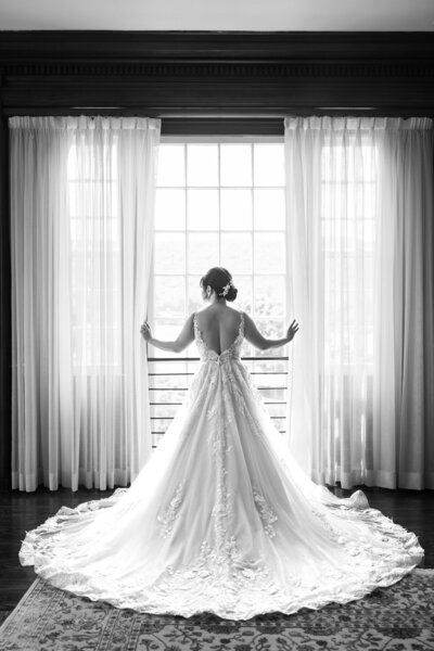 A black and white photo of bride standing in front of window