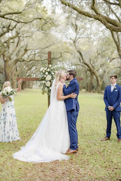 Bride and groom kiss during their Charleston wedding ceremony next to cross with flowers