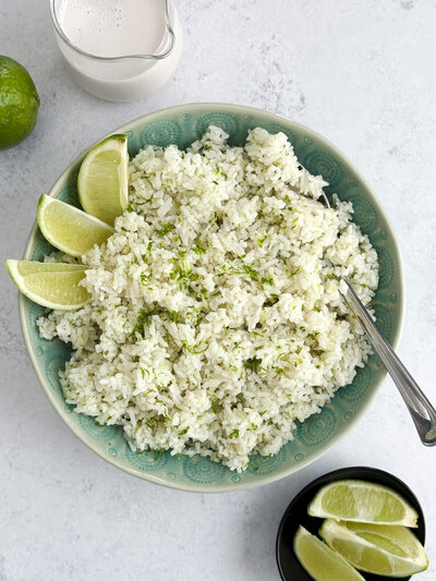A turquoise bowl of coconut lime rice toped with lime zest and fresh lime slices.