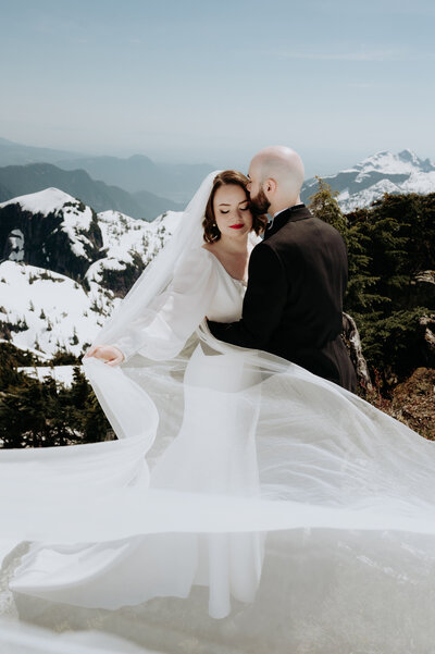 Bride getting kissed on a snowy mountaintop