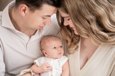 Newborn foto waarin ouders samen hun baby vasthouden en beiden liefdevol naar hun kleintje kijken – intiem en tijdloos vastgelegd door Juliette Fotografie.