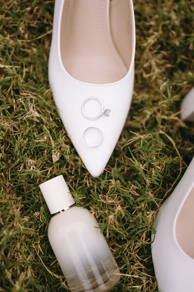 Fashion-forward bridal flat lay featuring pointed white heels, luxury fragrance, and wedding rings, styled by editorial wedding photographer Madison