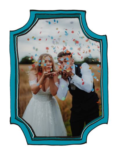 Bride and groom stood in a field blowing colourful confetti into the camera