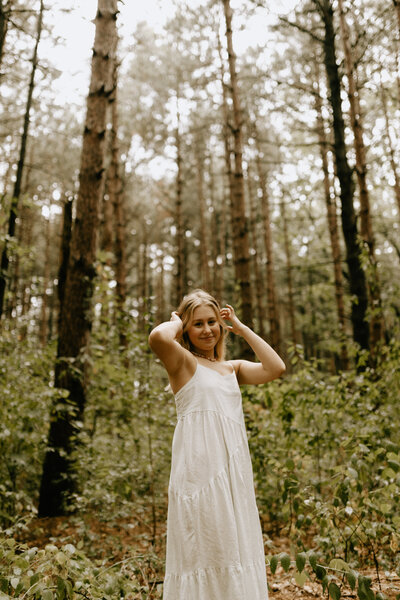 A girl standing in a green forest with her hands in her hair