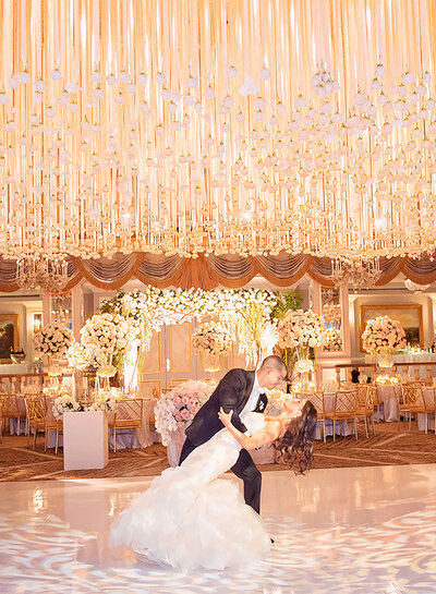 Groom dipping bride under ornate lights and hanging flowers