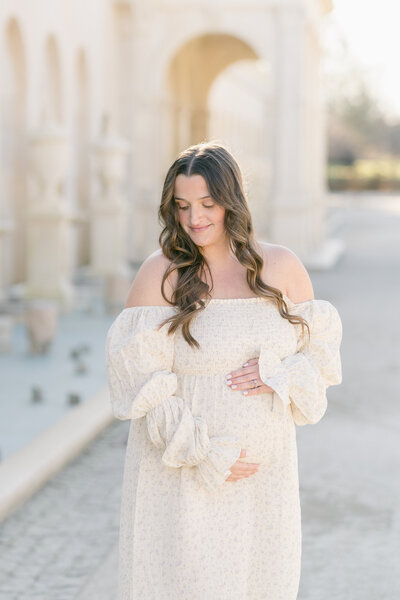 A pregnant woman wearing a white dress looks directly into the camera.
