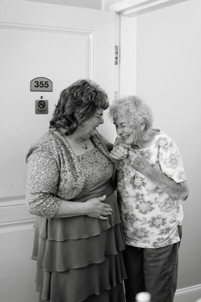 Two older women standing close together and laughing.