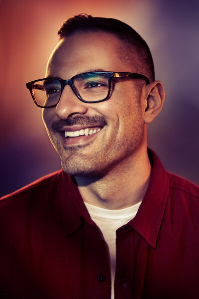 Stylish portrait of Mike Moretti with a warm smile, featuring vibrant lighting and a casual look, captured by Ylva Erevall.