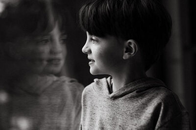 Young boy smiles out a window with reflection visible, candid family moment in Breckenridge.