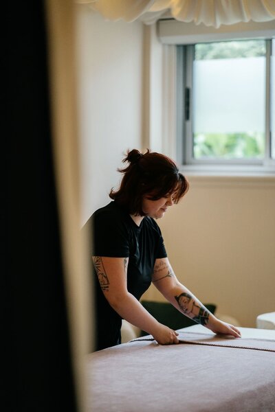 Tokalie, praticienne bien-être chez Maison Tokama à Rennes, prépare le lit de massage dans une cabine apaisante.