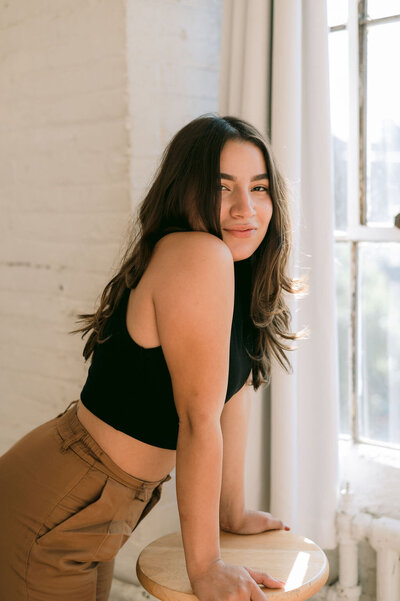 woman leaning on a stool with both hands while looking to the side smiling