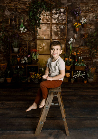 Little boy sitting on a ladder with a Spring backdrop in a photography studio