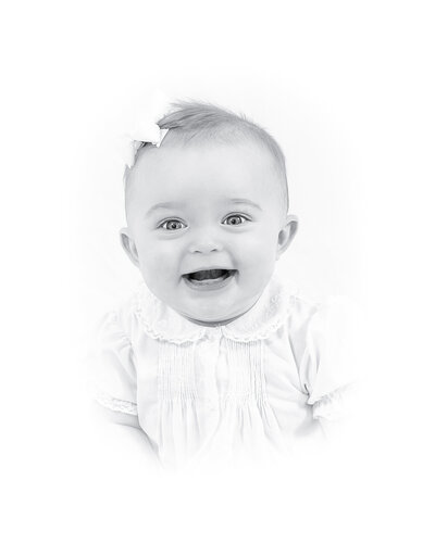 Black and white heirloom portrait of a smiling baby dressed in a classic white outfit with lace details. This timeless baby photography captures the innocence and joy of childhood, created by a Birmingham newborn photographer specializing in elegant, light-filled portraits.