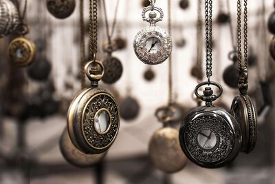 An assortment of vintage pocket watches with intricate designs hanging on delicate chains, displayed against a blurred backdrop.