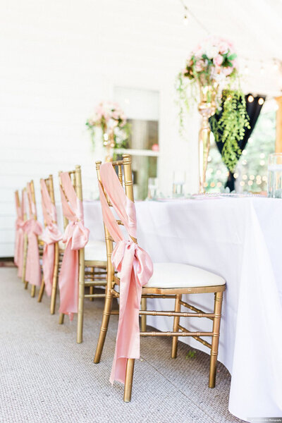 Elegant chairs with pink ribbon sashes set up for a wedding reception