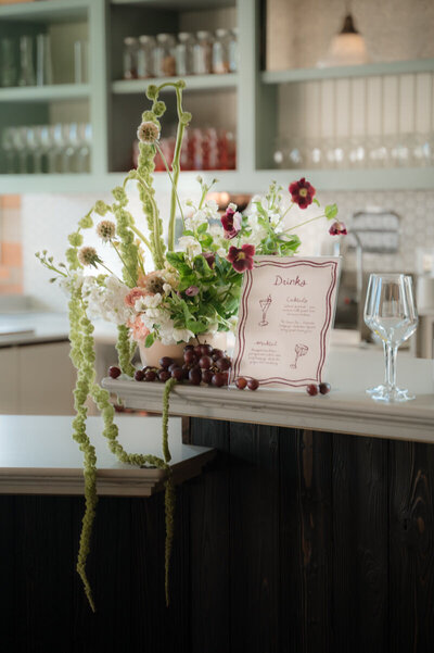 Specialty wedding cocktail menu next to an artful floral arrangement