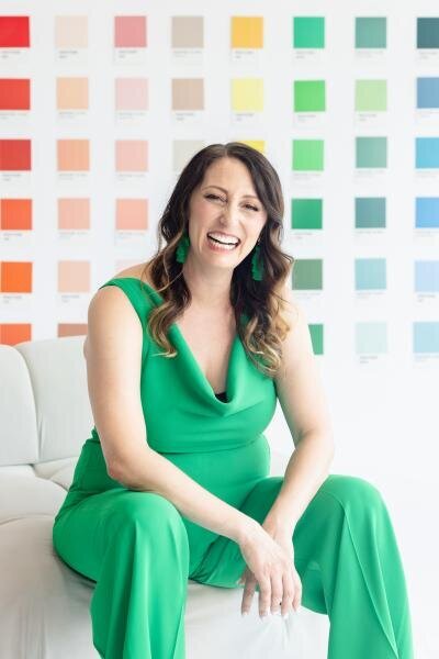 Brand strategist in vibrant green dress and matching earrings laughing authentically against color psychology wall featuring curated Pantone swatches
