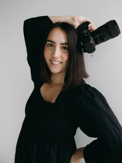 Ryann smiling with a camera, Indiana-based wedding photographer passionate about capturing love stories locally and worldwide.
