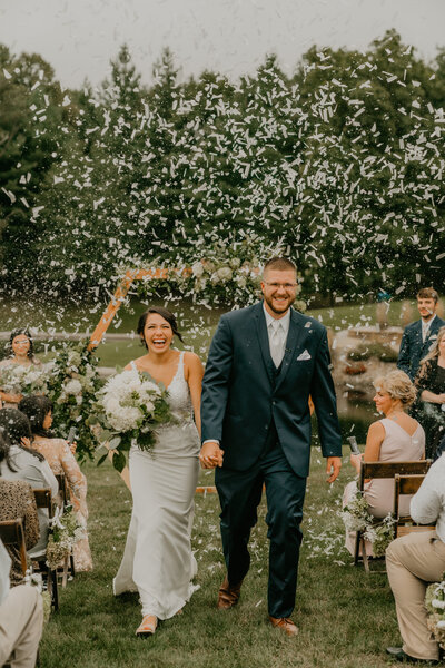 bride and groom walking down the aisle after getting married with confetti in the air