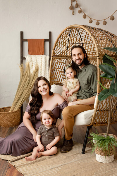 Family of four sitting and posing for the camera in a boho setting inside a St Louis photo studio