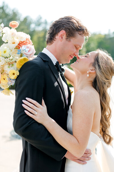 Bride and groom with their faces close together while bride holds her bouquet over groom's shoulder