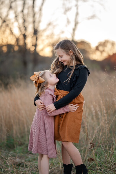 Sisters look at one another while the sunsets in an open field in the Fall