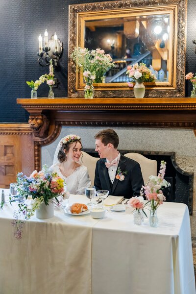 Bride & Groom tenderly smiling at each other during their reception while they are seated at their table at the Spokane Glover Mansion Wedding venue 
