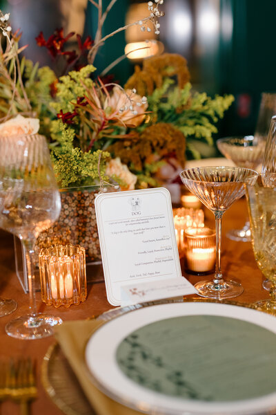 Grey Cove Designs custom wedding tablescape featuring candlelight, lush floral centerpieces, and an elegant dinner menu with classic serif typography displayed in a gold rimmed place setting.