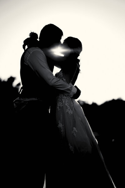 bride and groom kissing at sunset. They are in silhouette.