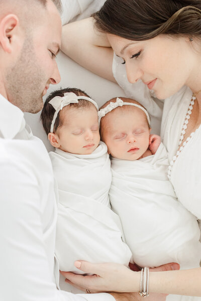 Mother and father look lovingly down at their newborn twin baby girls during newborn photography session
