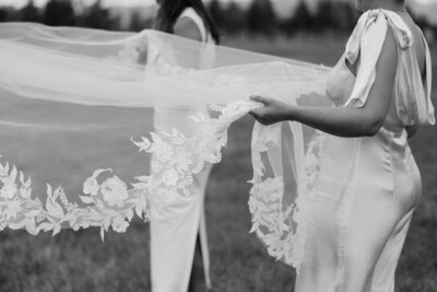 Black and white photo of bridesmaids holding a bride’s veil before the ceremony.