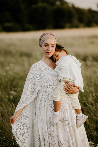 en kvinna med hijab håller om sin dotter i famnen på ett fält under en familjefotografering