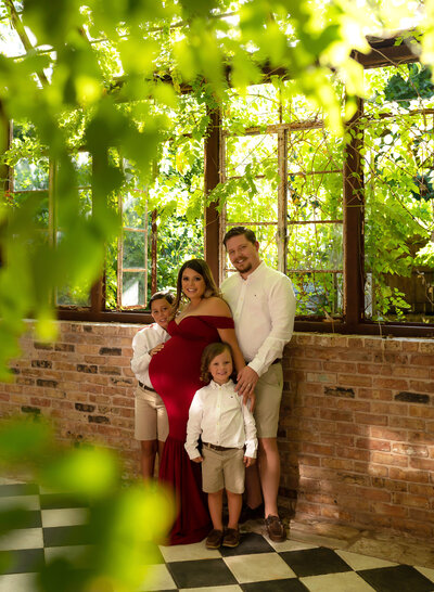 family of 4 with pregnant mom wearing red in greenhouse'