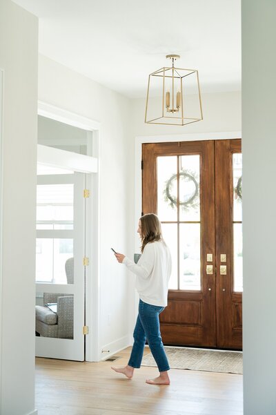 woman in a white sweater and blue jeans walks across a foyer in her home for candid branding photos