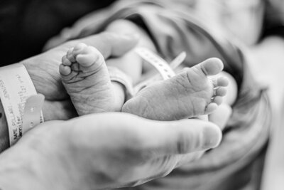 Newborn baby's feel being held by dad's hands. 
