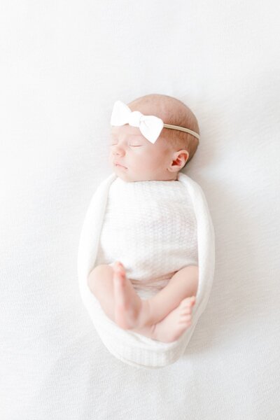 A newborn baby in a white onssie sleeps during photos. 