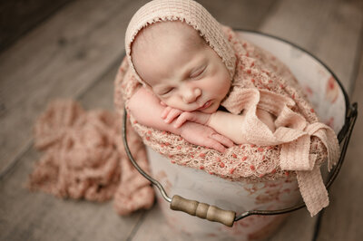 Newborn wrapped in pink blankets and floral blankets in a bucket
