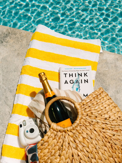 Beach bag filled with items sitting on a yellow striped towel laying next to the pool